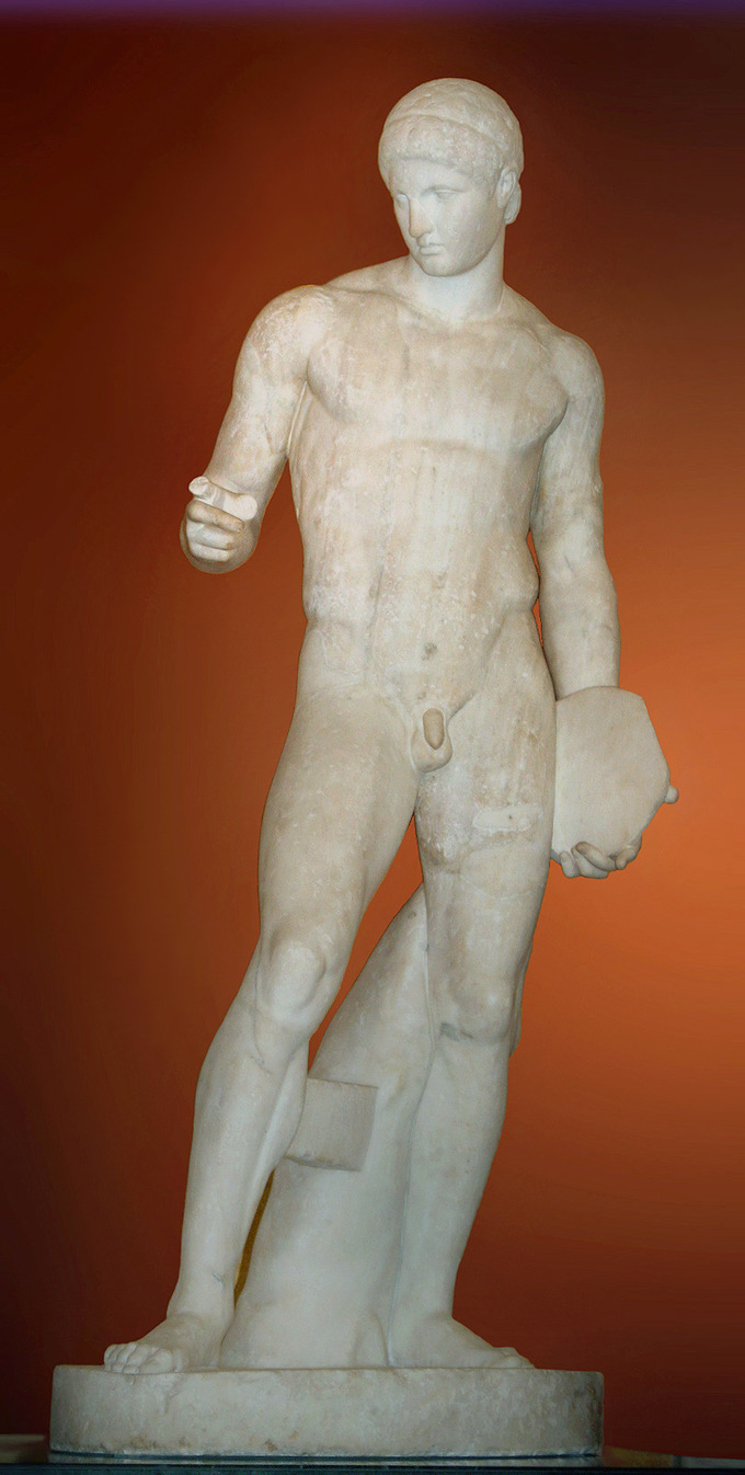This is a photo of Discophoros. It is a marble statue of a nude male figure with an idealized body (i.e., extremely defined muscles). Her gazes downward and raises an index finger, pointing.