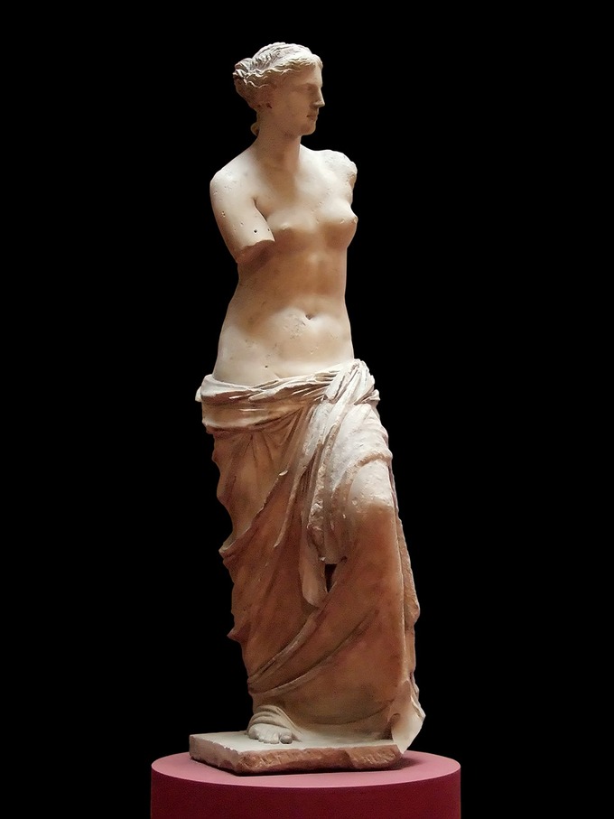 This is a photo Venus de Milo, and it is believed to depict Aphrodite, the Greek goddess of love and beauty. The statue depicts a woman's face in profile view and a body in frontal view. She is nude from the waist up. She has idealized abdominal muscles, and her lower body is clothed in draped fabric. She is missing both her arms.