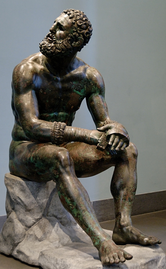 This is a photo of the bronze statue, Seated Boxer. That statue depicts a sitting nude boxer at rest, still wearing his caestus, a type of leather hand-wrap. He appears to be looking up and behind him.