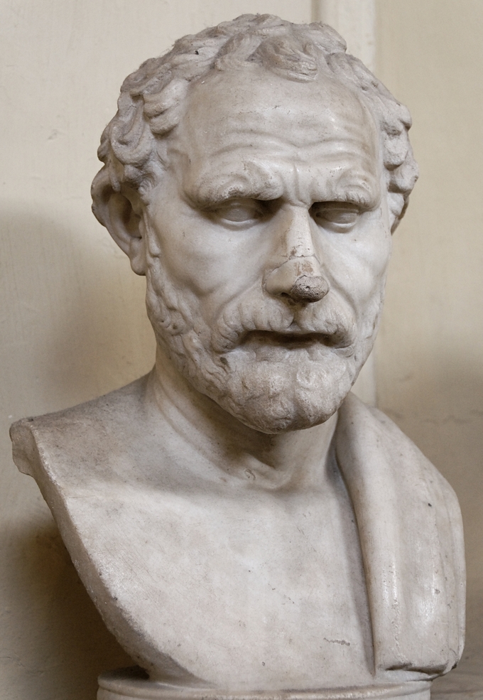 This is a photo of the portrait bust of Demosthenes, a bearded man with wavy hair and a receded hairline. His forehead is wrinkled and his eyes are closed.