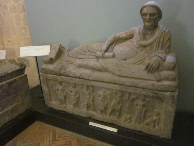 This is a photo of the Sarcophagus of Lars Pulena. The sculpted scene on the front of the coffin shows the deceased in the Underworld between two Charuns. On the lid, Pulena is shown laid across, in a reclining position, resting on his left arm and in front of him, a list of his life’s achievements which were inscribed on an open scroll.