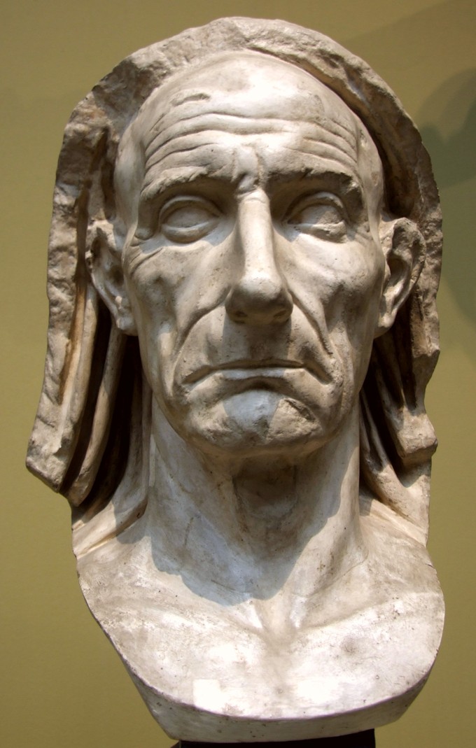 This photo shows the Bust of an Old Man. His face is realistic and life like with deep wrinkles in his forehead, crow's feet wrinkles around his eyes, and deep lines around his mouth.