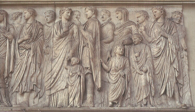 This photo shows a detail from the processional scene on the south wall of the Ara Pacis Augustae. It shows members of the imperial household, including adults and small children. They are dressed tunics and togas.