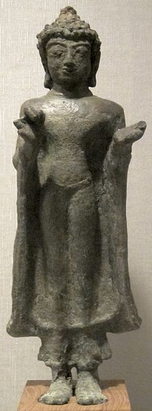 This photo shows a bronze statue of a standing Buddha. Sculpted in the Mon Dwaravati style, this bronze statue from the 7th century has an idealized rather than realistic physical form, including shell-like curls for hair.