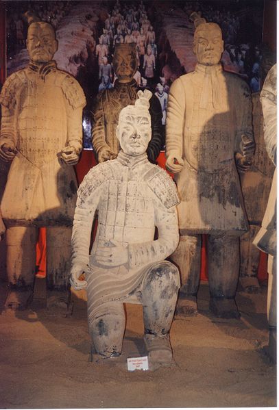 Photo of four figures from the Terracotta Army. Three are standing up straight and one kneels on one knee in front of them.