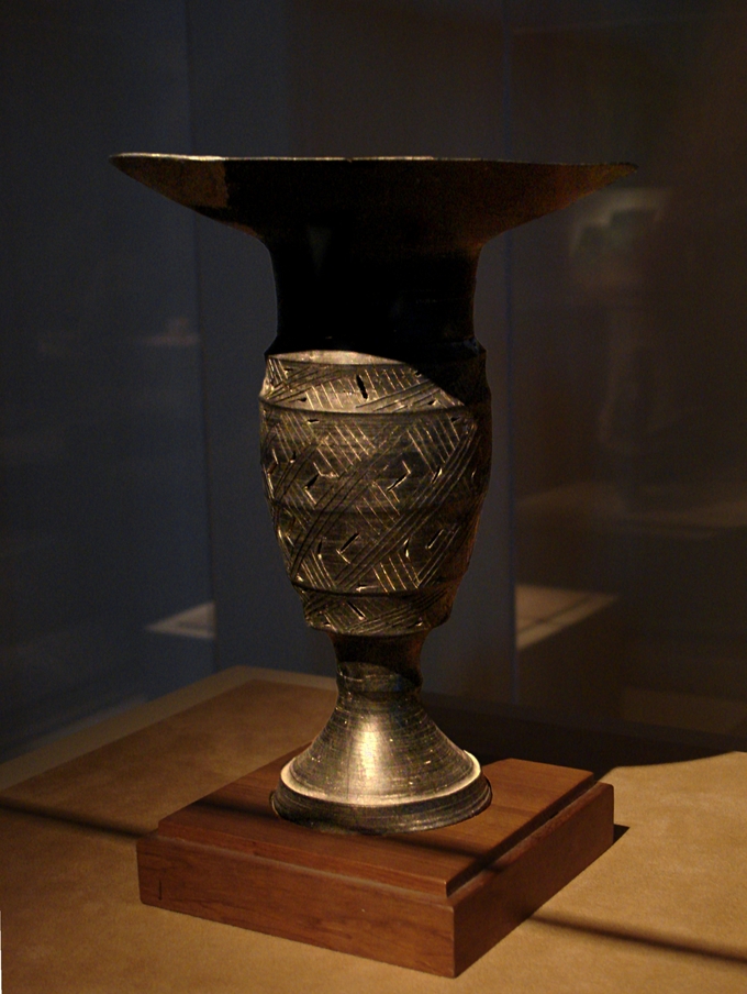 A vase, partially hidden in shadow, with decorative, weaving lines.