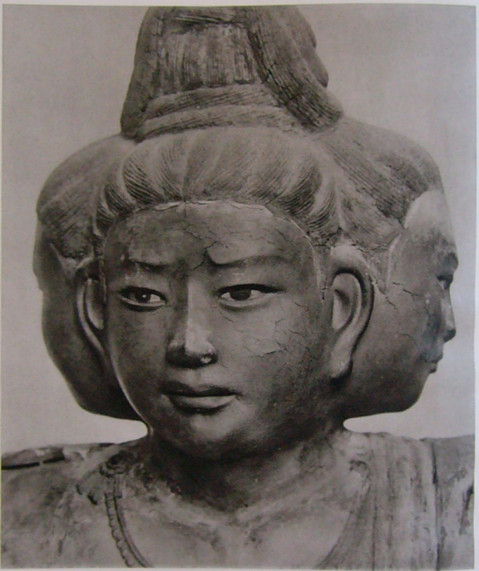 La escultura representa a un ser con varios rostros humanos, cada uno mirando una dirección diferente.
