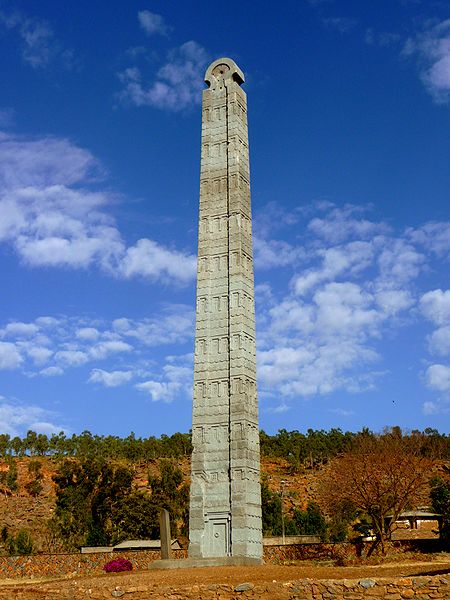 El obelisco está adornado con una puerta falsa en la base y presenta decoraciones que se asemejan a ventanas en sus lados. El obelisco termina en una parte superior semicircular.