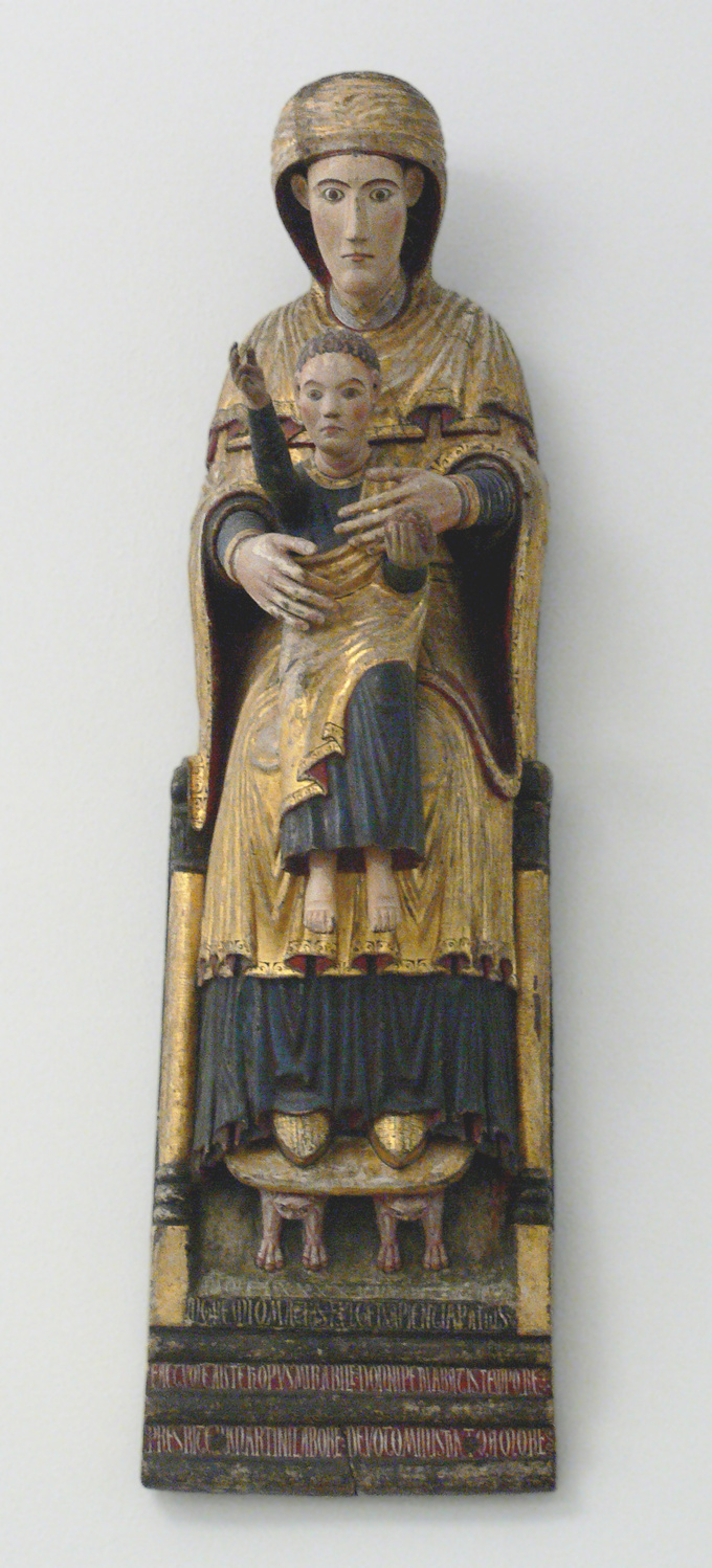 Sculpture of Mary seated on a throne holding the Holy Child in her lap. The figures are dressed in blue and gold and the Holy Child holds out his right arm.