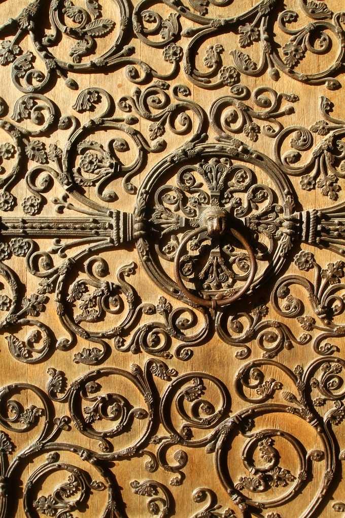 Image of an elaborately decorated door, featuring a lion's head door knocker in the center.