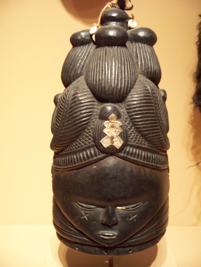 This mask has a face with a intricately carved headdress or hair.