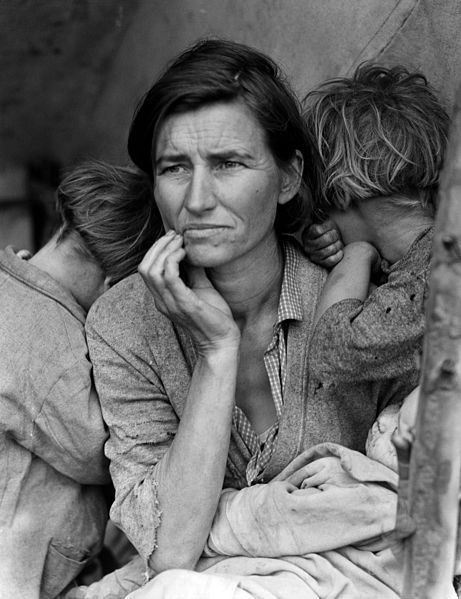 A sitting woman with a concerned expression holds a baby. Two children on either side of her hide their faces from the camera.