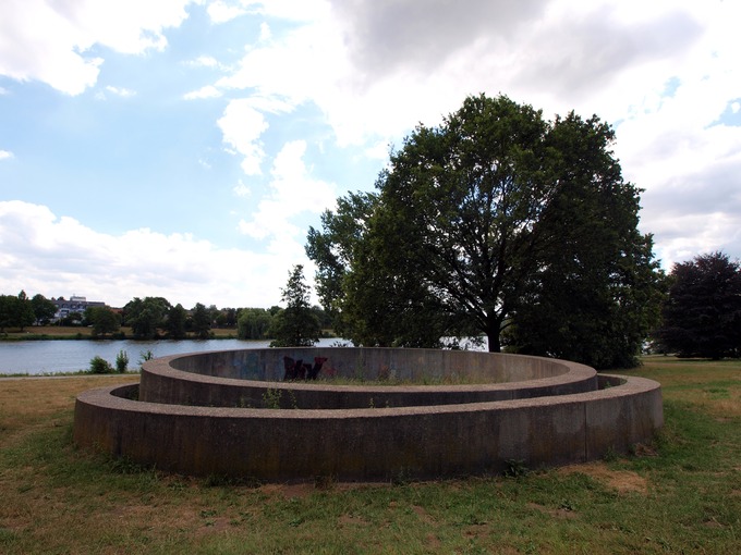 Un círculo de concreto colocado dentro de otro círculo de concreto. La escultura está afuera en un campo.