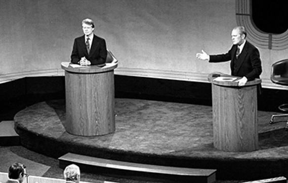 Una fotografía muestra a Gerald Ford y Jimmy Carter entablados en debate desde dos atriles. Ford está hablando y gesticulando hacia Carter con una mano.