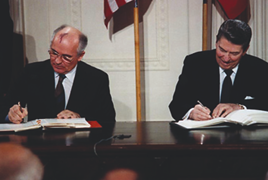 A photograph shows Mikhail Gorbachev and Ronald Reagan sitting beside one another as they sign the INF Treaty.