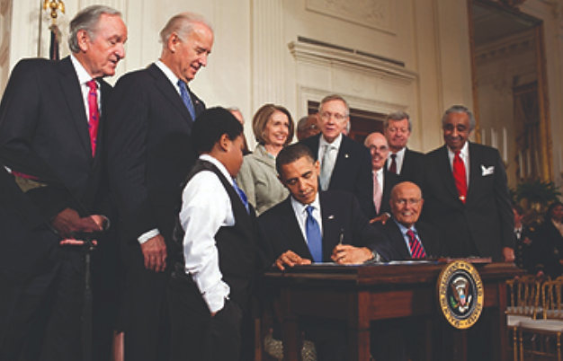 A photograph shows President Obama signing the Patient Protection and Affordable Care Act as Vice President Biden, Speaker of the House Nancy Pelosi, Senate Majority Leader Harry Reid, and others look on.