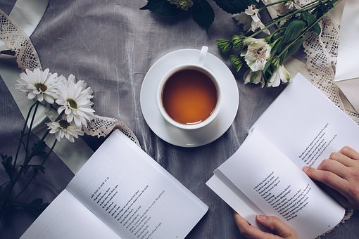 a cup of tea and some flowers next to an open book of poetry