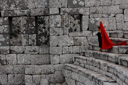 Mujer sosteniendo largo rojo capa tipo pieza de tela se encuentra sola en un anfiteatro de piedra