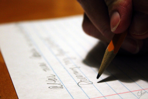 Photo of a hand holding a pencil, writing on a piece of notebook paper