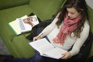 Woman sitting on a sofa with a statistics book next to her, reading another book.