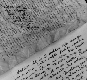 Photo of a crumpled piece of printed text with handwriting on top of it, lying over handwriting on a notebook page