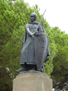 Photo of a statue outdoors, depicting a knight in chain mail, brandishing a sword and shield