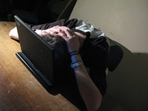 Student with his head on a laptop's keyboard, hands held behind his head in a gesture of frustration