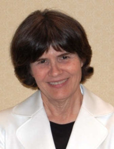 Head-shot photo of a woman with brown hair, smiling into the camera. She is wearing a white jacket and black shirt.