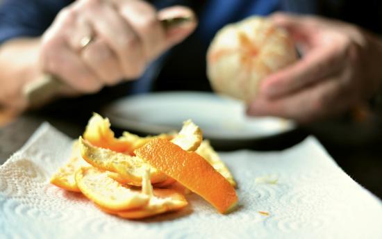 A person peeling an orange. The orange peels are in the foreground. 
