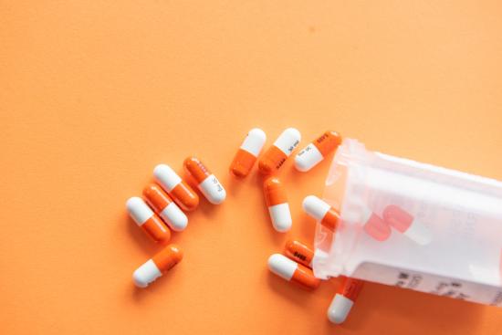 orange and white pills spilling out of a pill container 