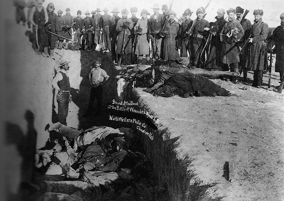Burial of the dead after the massacre of Wounded Knee. U.S. Soldiers putting Indians in common grave; some corpses are frozen in different positions. South Dakota. 1891. Library of Congress.