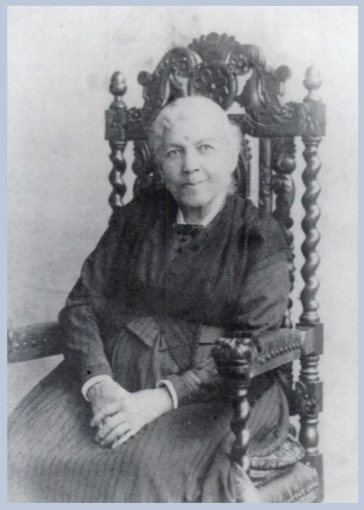 An older Harriet Ann Jacobs seated in a ornate carved wooden high chair, white hair, black dress, hands folded in her lap