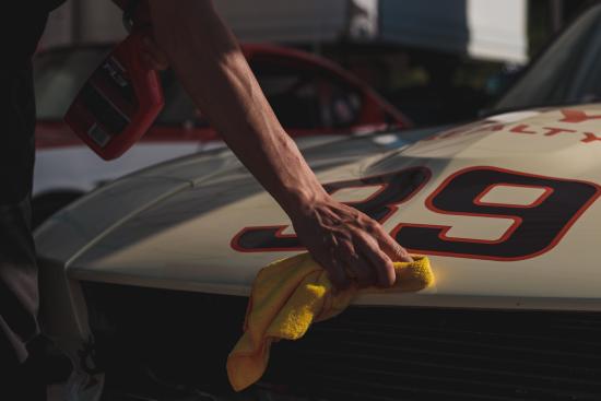 a hand cleaning the hood of car with a yellow rag