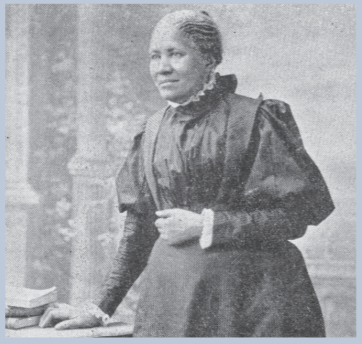 Photograph of Frances Ellen Watkins Harper standing with her right hand on a desk and her left in front of her waist. Natural short grey hair, black dress.