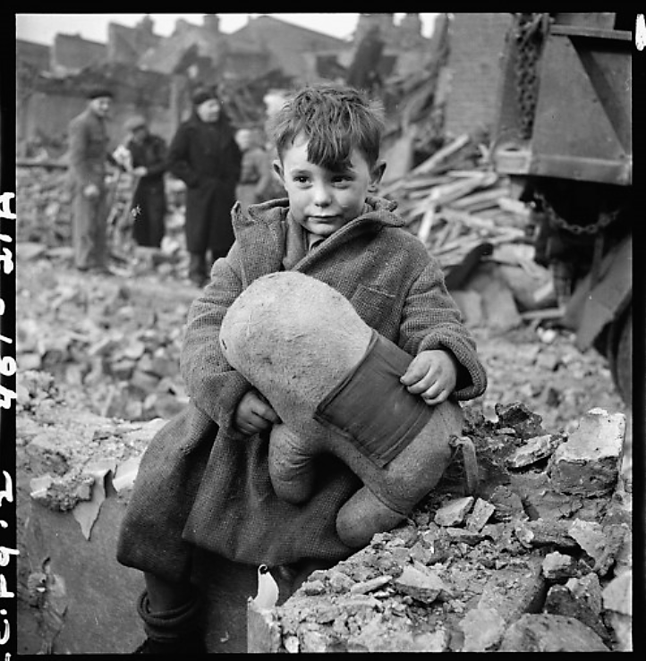 The German aerial bombing of London left thousands homeless, hurt, or dead. This child sits among the rubble with a rather quizzical look on his face, as adults ponder their fate in the background. Toni Frissell, “[Abandoned boy holding a stuffed toy animal amid ruins following German aerial bombing of London],” 1945. Library of Congress, http://www.loc.gov/pictures/item/2008680191/.