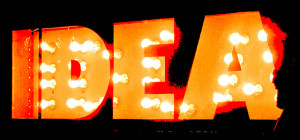Photo of a sign reading "IDEA." The letters are formed out of orange metal and lit up with exposed light bulbs, set against a black backdrop