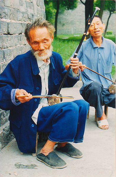 An old man on a street playing the erhu.