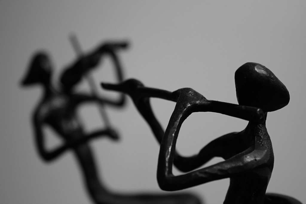 Photo of two small sculptures: a flute player in the foreground and violin player in the background.
