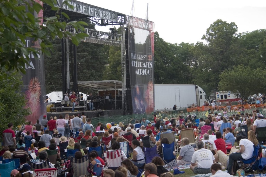Photo of outdoor concert and concertgoers sitting on the grass
