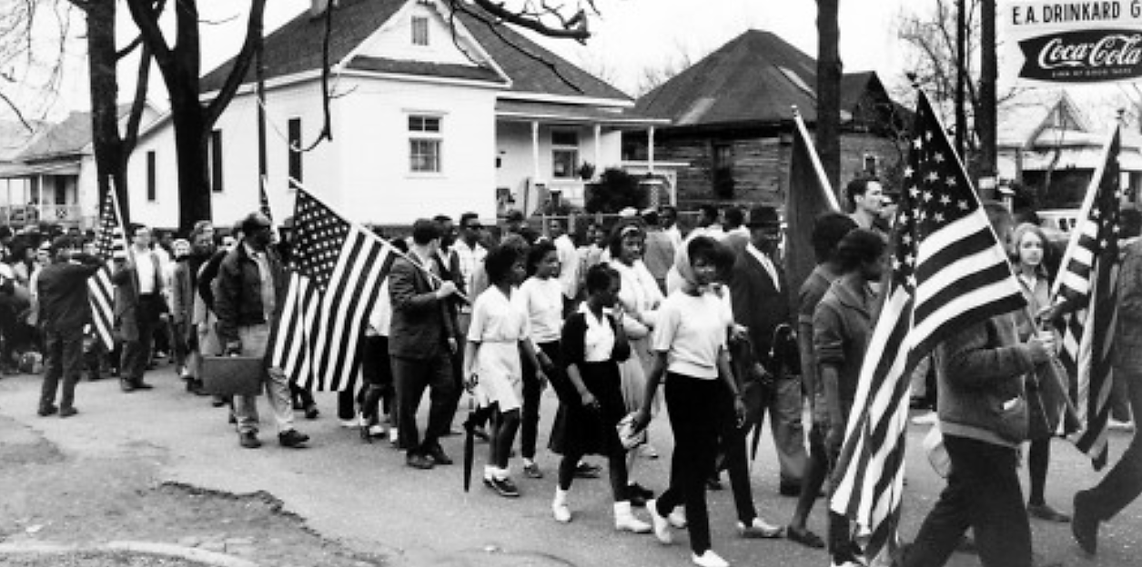 “Participantes, algunos portando banderas estadounidenses, marchando en la marcha por los derechos civiles de Selma a Montgomery, Alabama en 1965”, vía Biblioteca del Congreso.