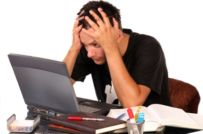 A stressed out student staring at his computer with his hands on his head.