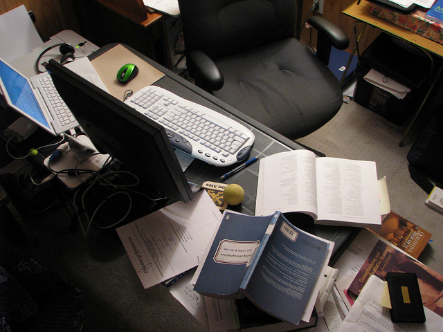 A computer desk with books scattered everywhere in a disorganized mess.