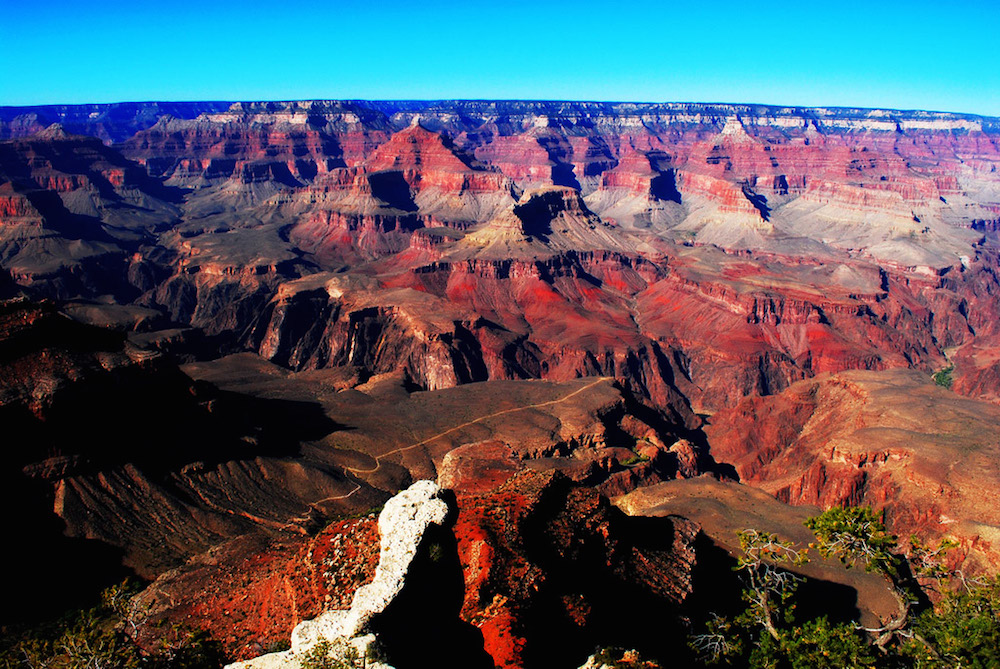 An image of the Grand Canyon. The formations of rock reveal colored patterns at different layers.
