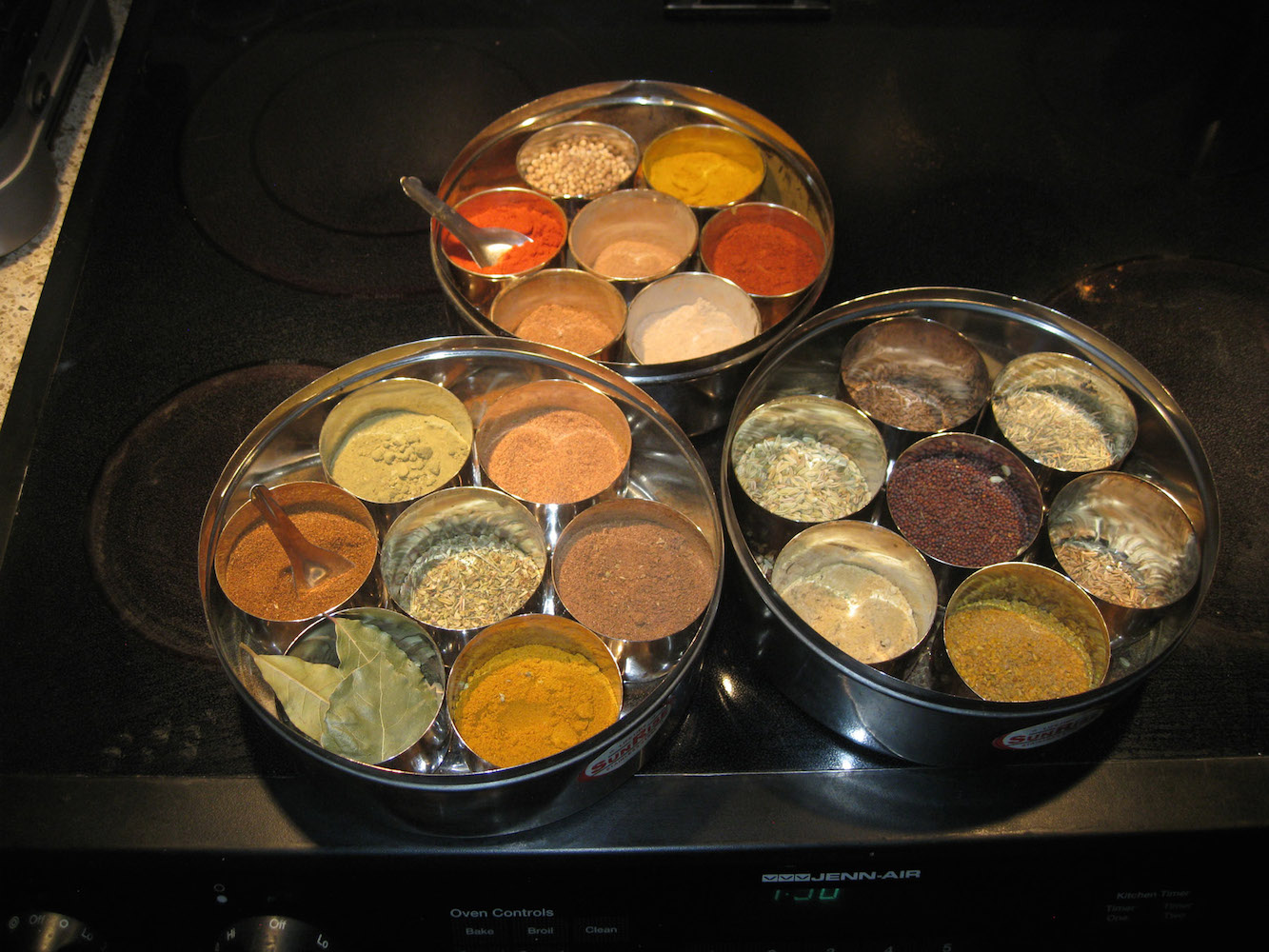 A picture of three round containers, each of which contains seven round containers filled with spices.