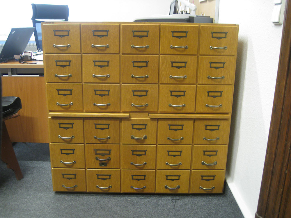 Photo of a wooden card catalog cabinet. Six drawers high; five drawers wide; two drawers extendable from mid-cabinet. The material appears to be oak.