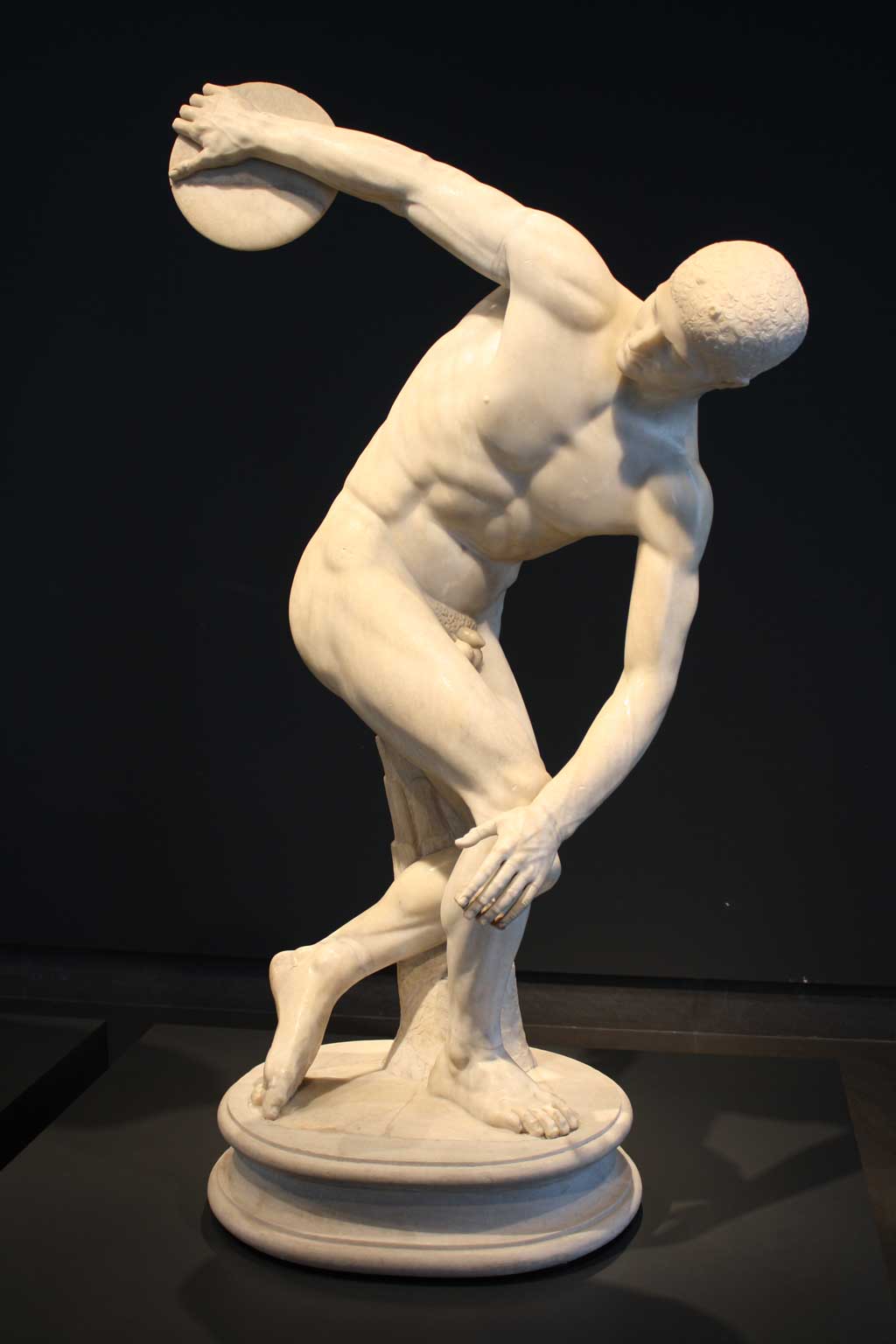 Image of the Discus Thrower. A marble replica of the original, the statue depicts a stoic-faced athlete in mid-rotation as he prepares to hurl the discus aloft.