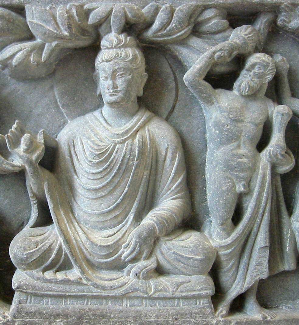 Stone relief of the Buddha sitting in the lotus position with long flowing robes. Positioned to the Buddha's left is a strapping depiction of Hercules holding a mace in his right hand to signify his role as the Buddha's protector.