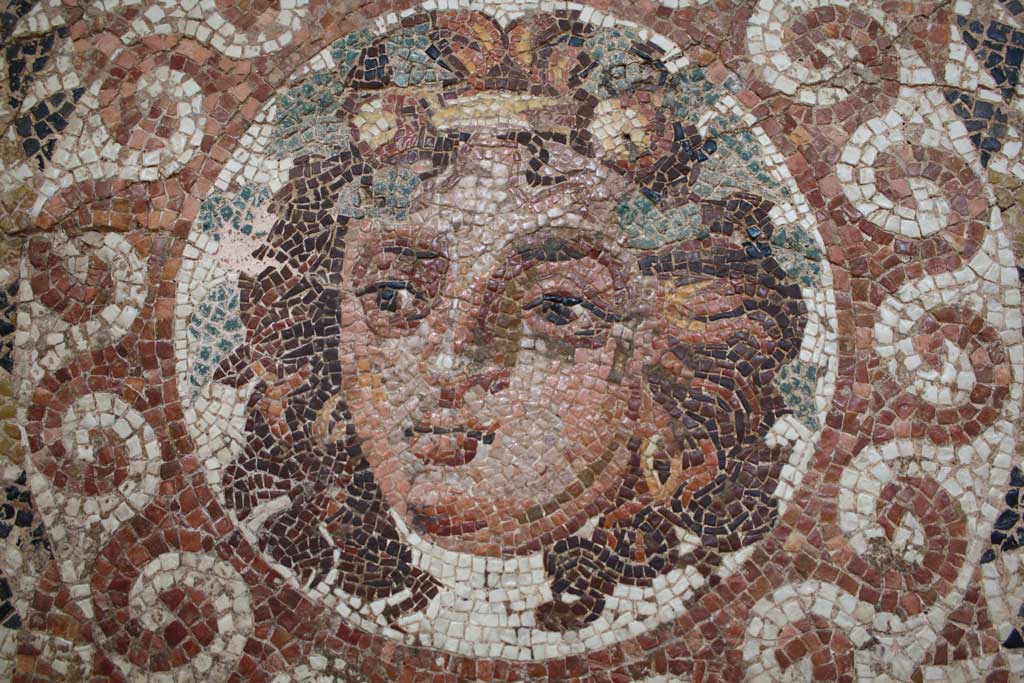 A tiled frieze of the bust of Dionysus. In this image, the viewer sees the long-haired deity with vines surrounding his head.