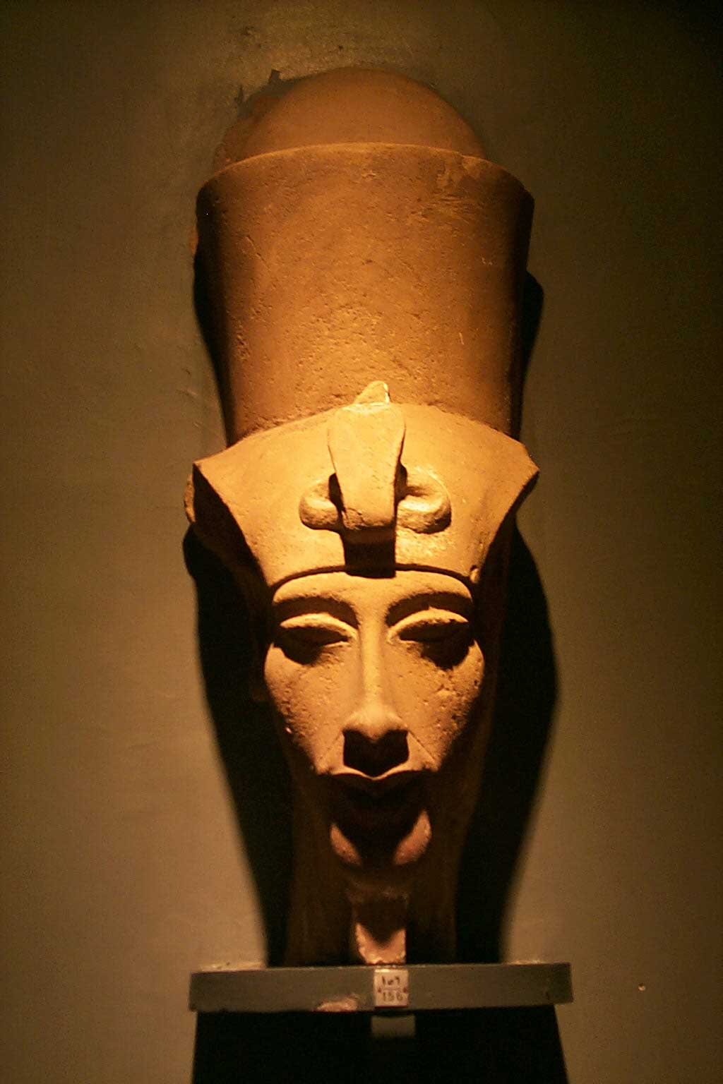 The picture is of a stone bust of Pharaoh Akhenaten. Here, the king is depicted with a slender face and extended facial features. Atop his head is the double crown of Egypt.