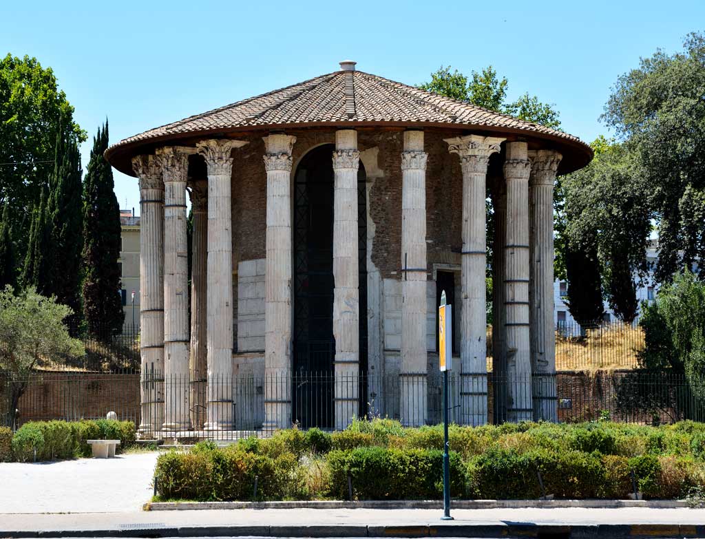 This photo shows the ruins of the Temple of Hercules Victor. It is a circular facility with a slanted rounded roof. It is surrounded by columns on a platform.